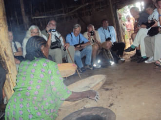 9 people indoors watching a Sidama woman demonstrating preparation food from enset